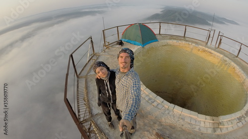 Camping on top of a smoke stack chimney, surrounded by fog and mist underneath the top of the building, sunrise