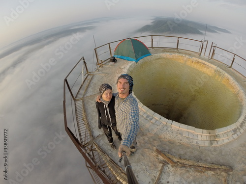 Camping on top of a smoke stack chimney, surrounded by fog and mist underneath the top of the building, sunrise