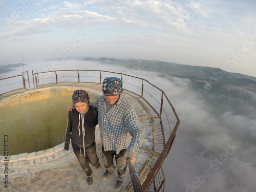 Camping on top of a smoke stack chimney, surrounded by fog and mist underneath the top of the building, sunrise
