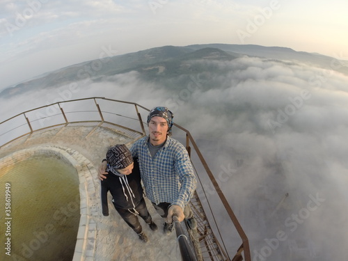 Camping on top of a smoke stack chimney, surrounded by fog and mist underneath the top of the building, sunrise