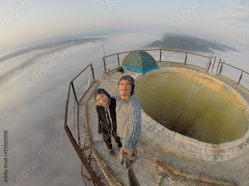 Camping on top of a smoke stack chimney, surrounded by fog and mist underneath the top of the building, sunrise
