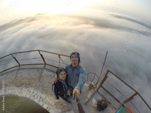 Camping on top of a smoke stack chimney, surrounded by fog and mist underneath the top of the building, sunrise