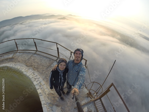 Camping on top of a smoke stack chimney, surrounded by fog and mist underneath the top of the building, sunrise