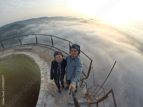 Camping on top of a smoke stack chimney, surrounded by fog and mist underneath the top of the building, sunrise