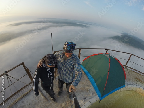Camping on top of a smoke stack chimney, surrounded by fog and mist underneath the top of the building, sunrise