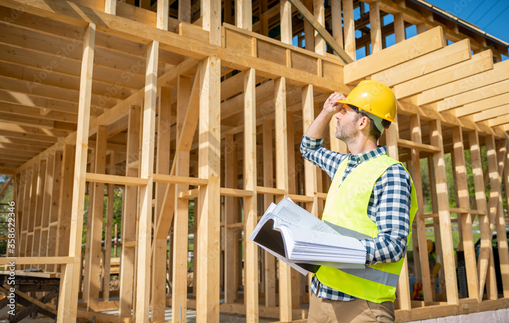 Fototapeta premium Construction engineer or architect with blueprints visiting building site of wood frame house