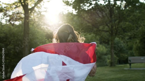 A woman runs for joy with a Canadian flag behind her for independence day. Slow-motion flowing in the breeze and shot in 4k.