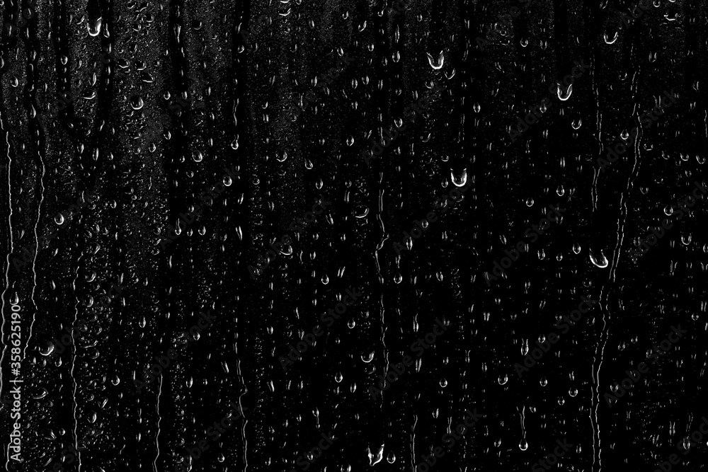 Drops of water flow down the surface of the clear glass on a black background. Texture for creativity.