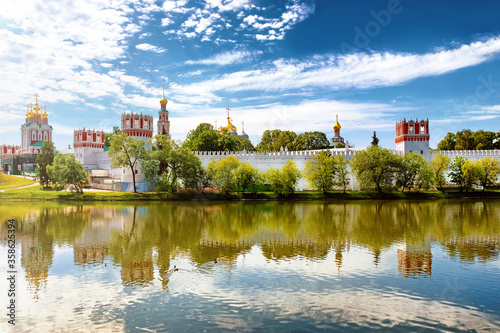 famous moscow city novodevichy convent landmark with golden domes and scenery reflection on park pond water against scenic blue sky with clouds background. Wide view