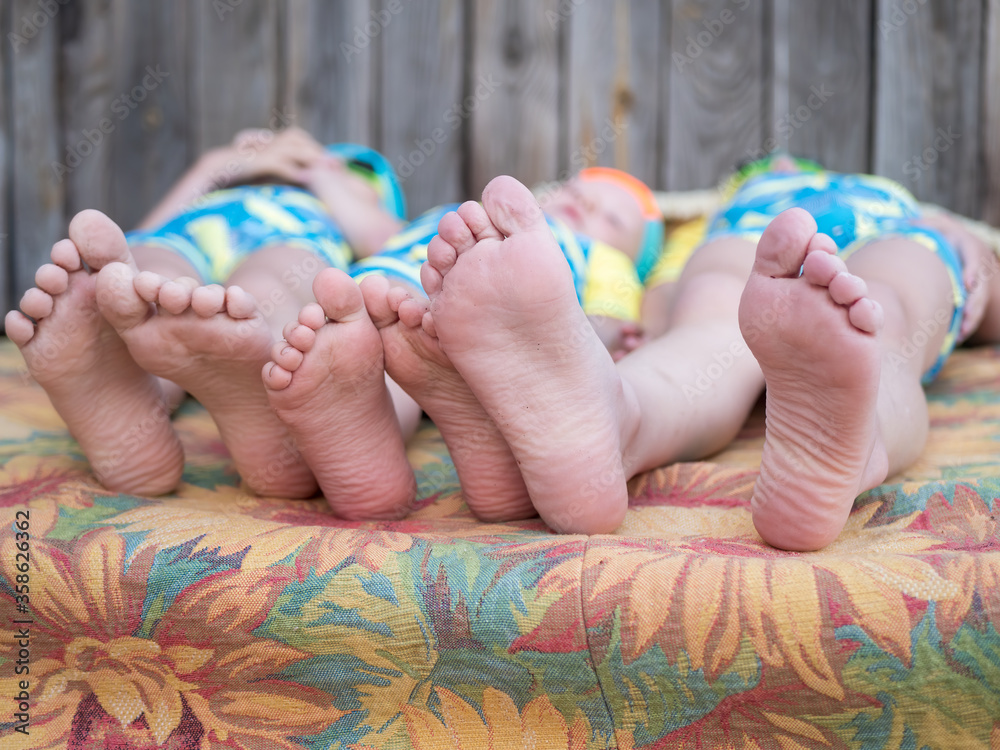 Naklejka premium Funny children in swimsuits lie together on mattress after swimming in pool. boys are happy on vacation in village together. Summer day, river, swimming in water. Close-up of legs and feet