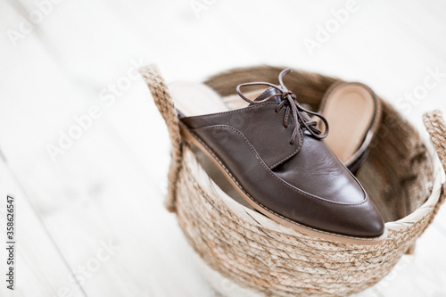 brown leather shoes for women without a heel lie in a wicker basket of straw. Trending photo of spring autumn footwear. elegant flip flops.shoelaces