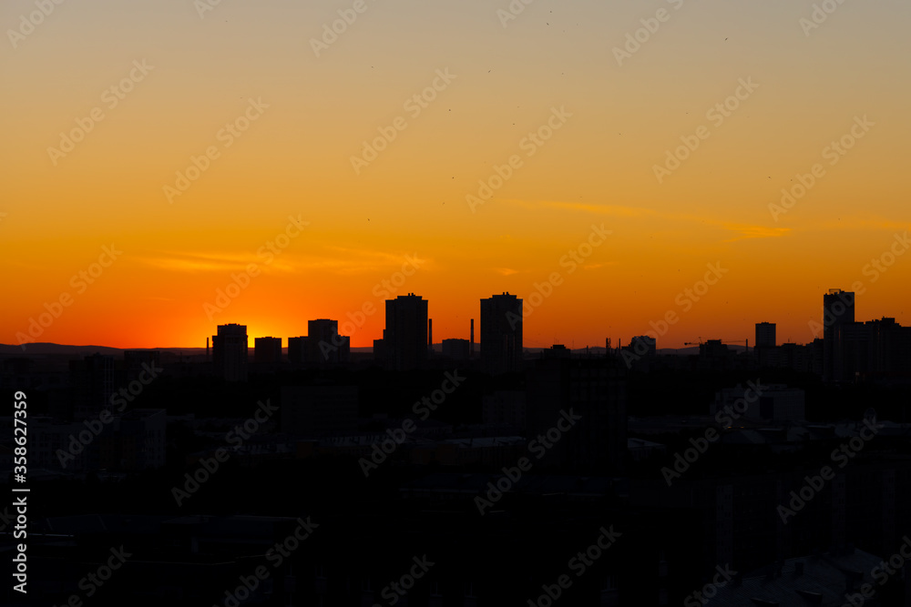 Black silhouettes of buildings are on a red sky background with orange and yellow sunset