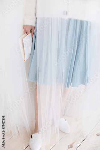 a girl in a skirt and shoes is reading a magazine, female slim legs in suede mules and flat loafers, a woman is sitting in a room on a sofa or armchair and is holding a cup and a magazine