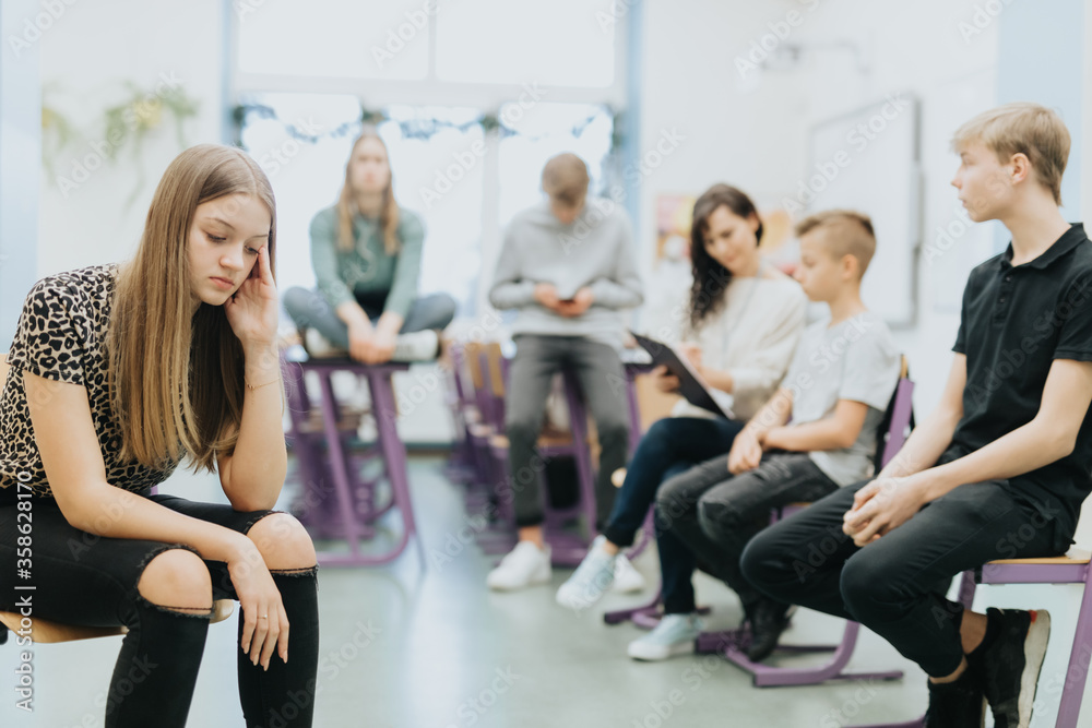 Beautiful thoughtful teenage girl sits on the side of a class during lesson at school
