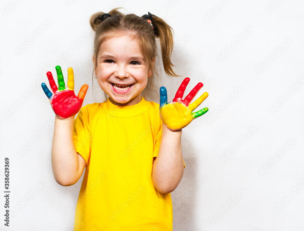 Beautiful little girl with hands in paint smiles in a yellow T-shirt. Children's creativity. Beautiful little girl with hands in paint smiles in a yellow T-shirt. Children's creativity.