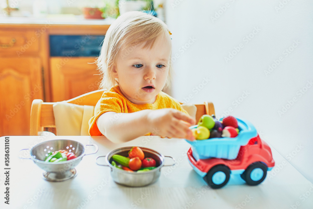 Adorable little girl playing with toy fruits and vegetables at home Adorable little girl playing with toy fruits and vegetables at home
