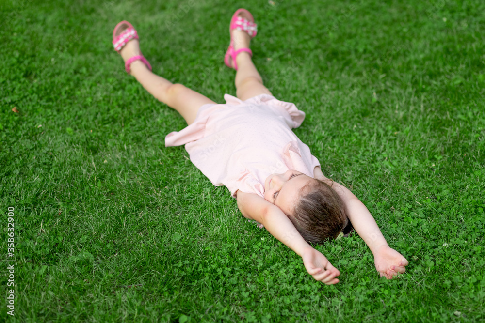 a 5-6-year-old girl lies on her back in the Park on the grass, happy childhood, child's day a 5-6-year-old girl lies on her back in the Park on the grass, happy childhood, child's day