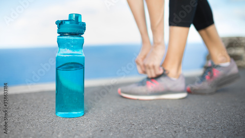 Fotografia Active female runner tying shoe next to bottle of water
