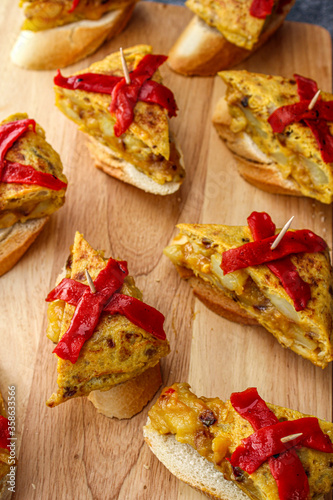 Spanish tortilla pintxo on a wooden board. Potato omelette on bread as a basque canape on sharing board. Party food. 
