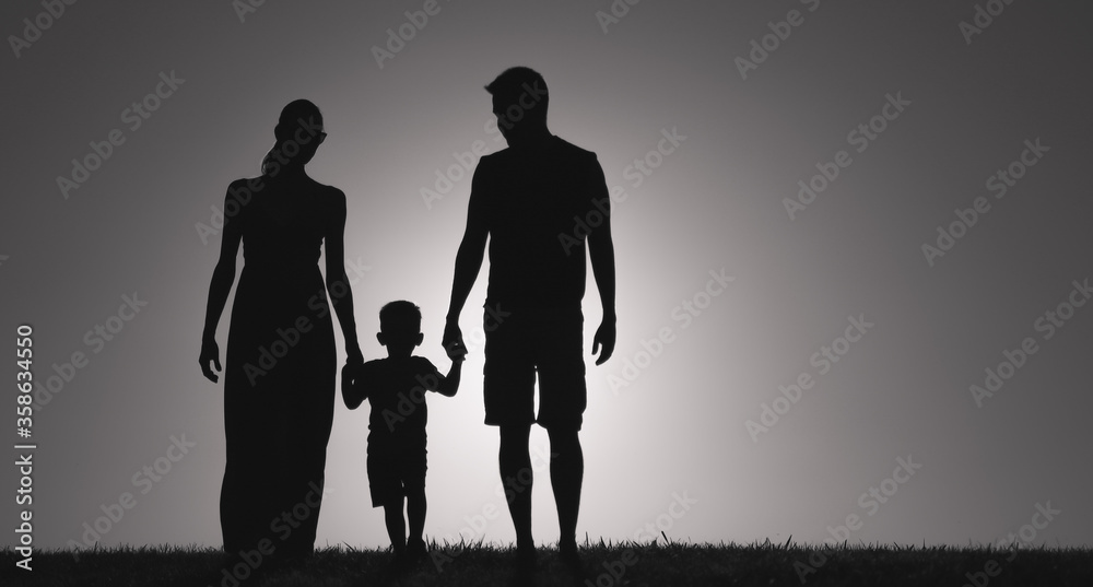 silhouette of child holding mother and father's hand walking together at sunset