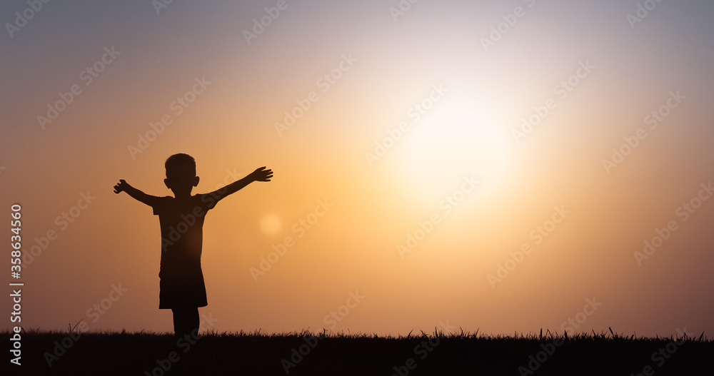 Silhouette of happy little boy with arms up in the sunset. 