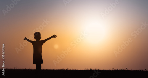 Silhouette of happy little boy with arms up in the sunset. 