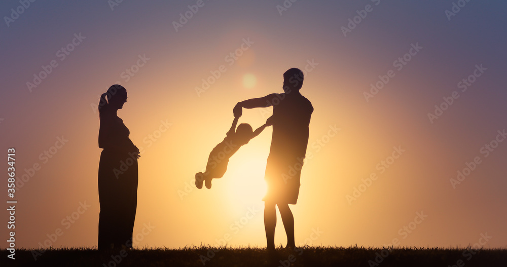 Silhouette of happy family playing together outdoors in the park.