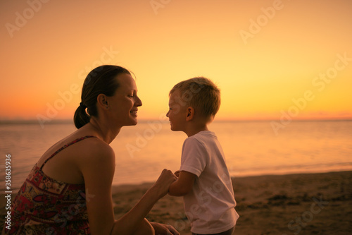 Happy mother and son smiling together on the beach at sunset. 