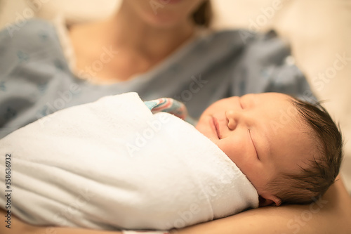 closeup portrait of newborn baby girl sleeping in mothers arms lying in hospital bed. 