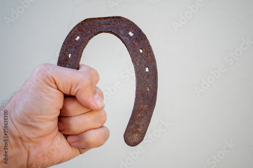 man hand holding old and rusty horseshoe with blurred white background and space for text