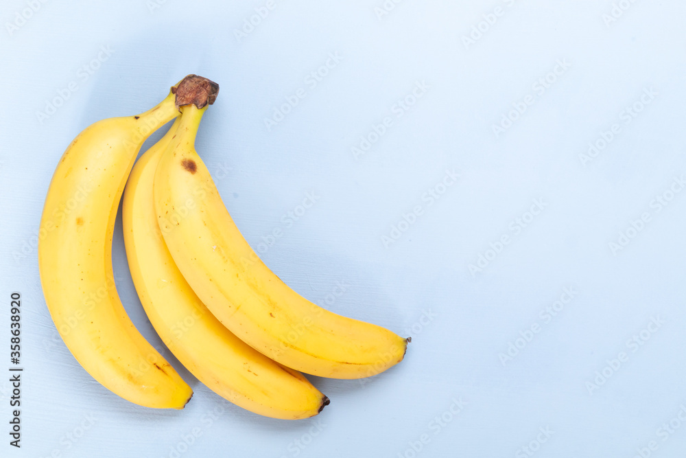 Bunch of fresh sweet organic bananas on light blue  background, empty space for text
