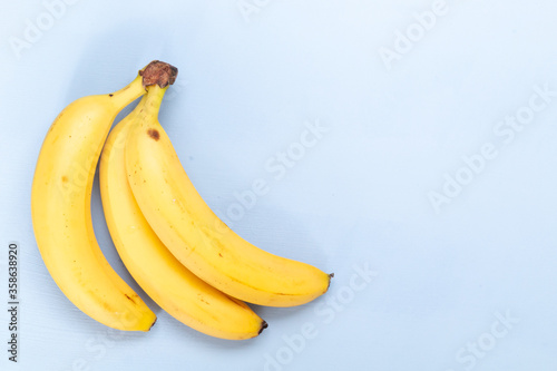 Bunch of fresh sweet organic bananas on light blue background, empty space for text 