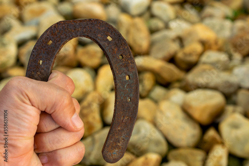 man hand holding old and rusty horseshoe with blurred stones background
