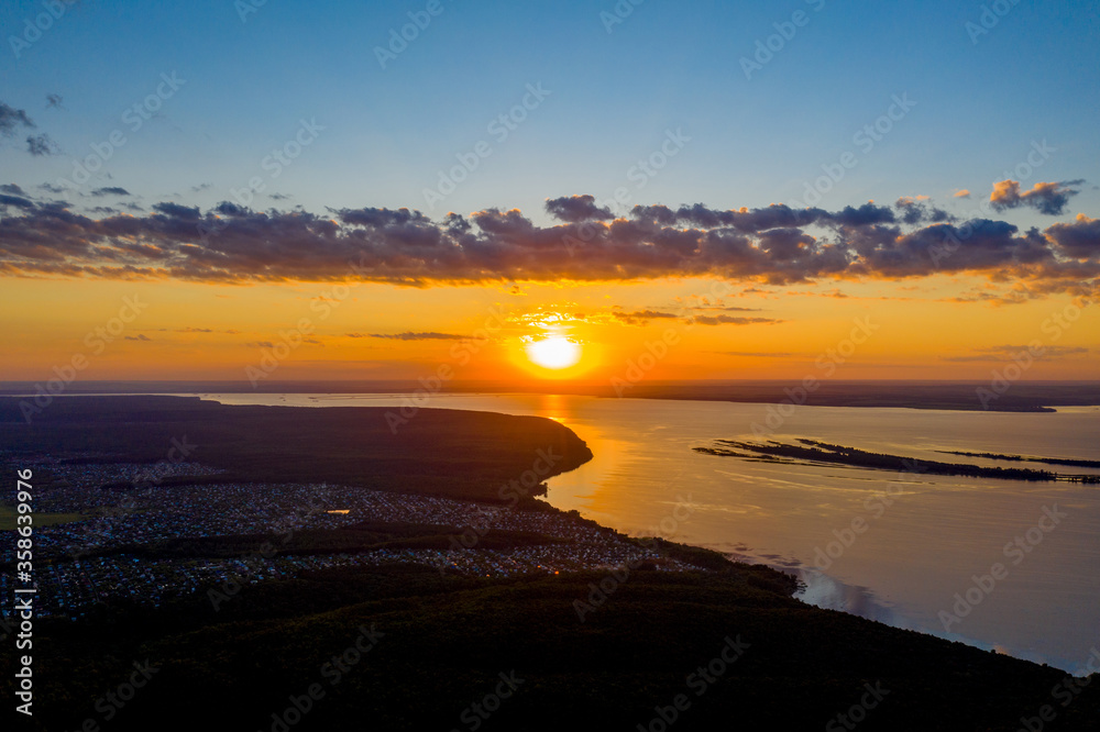 Obraz premium The setting sun over a wide, deep, flat river. There is a summer cottage village on the river Bank. Shooting from a drone. Copy space.