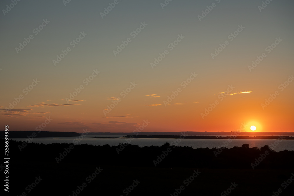 Summer landscape. Red sunset over a wide flat river with wooded banks. Copy space.