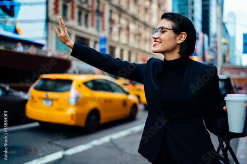 Fototapeta Cheerful successful woman hailing rideshare taxi car on road for getting to busi