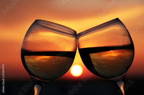 Two glasses with white wine on sunset background, evening sun is reflected in a glass. Concept of celebration, romantic evening, love date