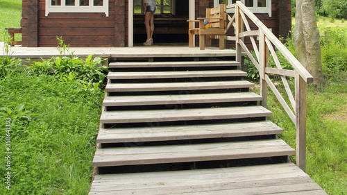 Empty outdoor wooden staircase steps in front of the cottage house against the background of green grass, close up bottom up view on a Sunny summer day, Russian natural landscape