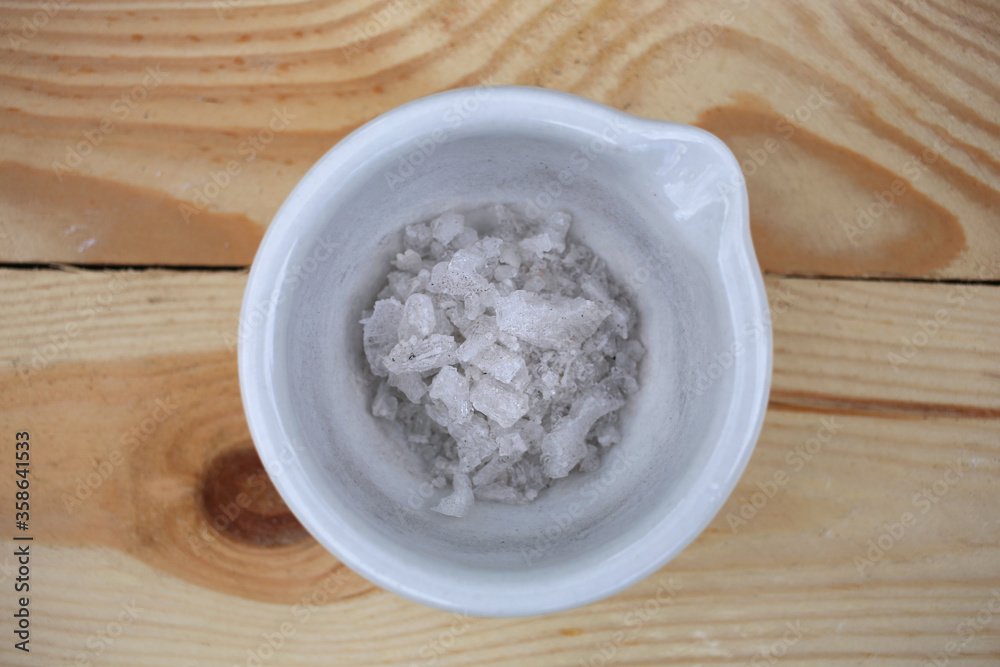 Large white crystals of potassium nitrate in a ceramic mortar, on a wooden table. Large white crystals of potassium nitrate in a ceramic mortar, on a wooden table.