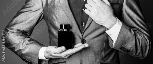 Fragrance smell. Men perfumes. Fashion cologne bottle. Men perfume in the hand on suit background. Man in formal suit, bottle of perfume, closeup. Black and white.