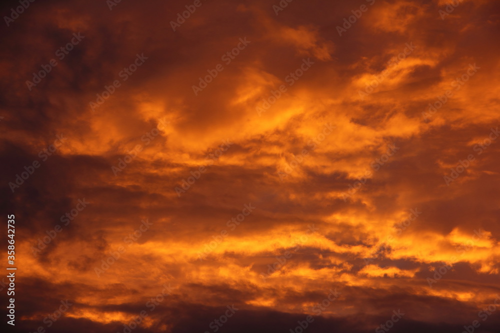 Orange colorful dramatic storm clouds on sunset with sun rays illumination in the sky close up on a summer evening, beautiful cloudscape, texture for background and wallpaper