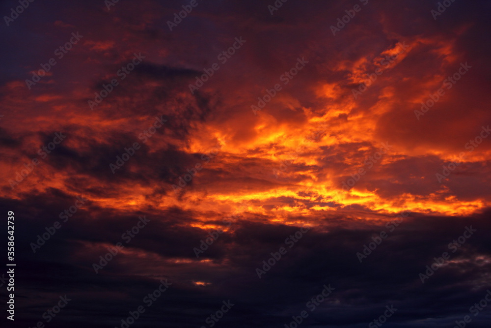 Heavy black orange colorful dramatic stormy clouds on sunset with sun rays lighted  sky on a summer evening, beautiful cloudscape view, texture for background and wallpaper