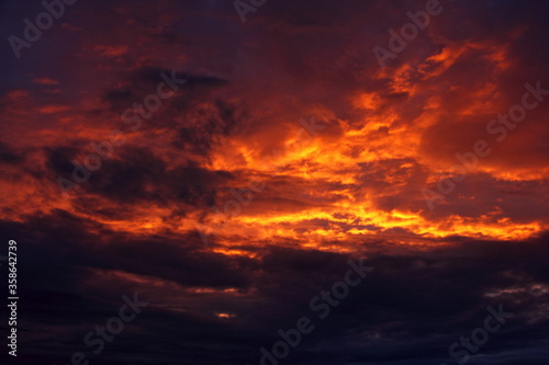 Heavy black orange colorful dramatic stormy clouds on sunset with sun rays lighted sky on a summer evening, beautiful cloudscape view, texture for background and wallpaper