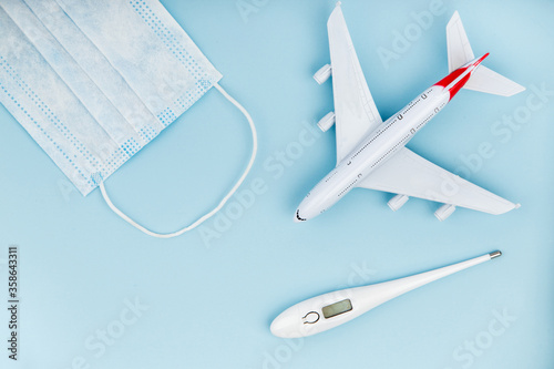 Airplane, medical mask and thermometer on a blue background.