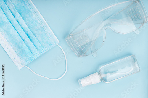 Hand sanitizer, medical mask and protective glasses on blue background.