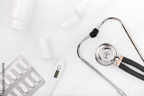 Stethoscope, thermometer and pills on white background.