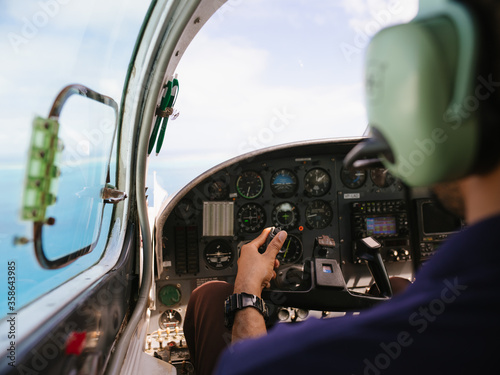 Fényképezés Over the shoulder of pilot flying a small plane over the ocean water with view o