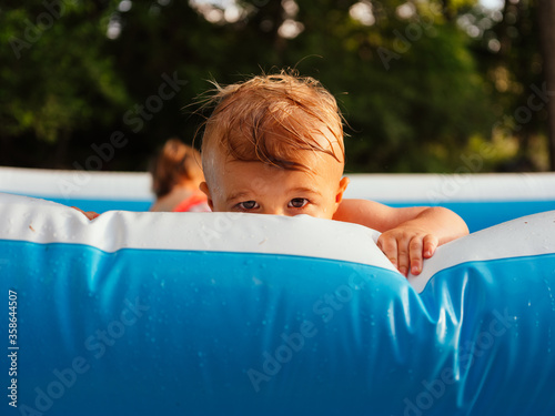 Slika na platnu Toddler boy peeks over the edge of a blowup pool, looking at camera