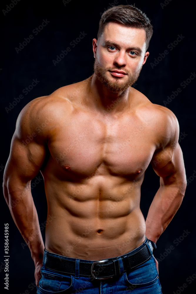 Handsome man with big muscles, posing at the camera on dark background. Portrait of a smiling bodybuilder. Closeup.