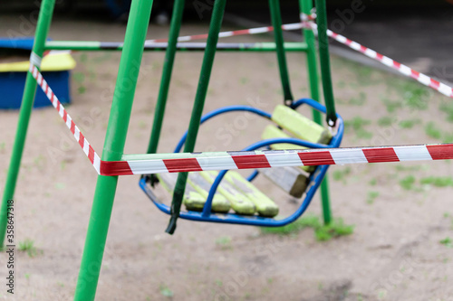 Yellow children's swing on a sports playground in the park wrapped with red barrier tape. Outside. Prohibition of outdoor walks, prevention of the coronavirus influenza virus covid-19. selective focus